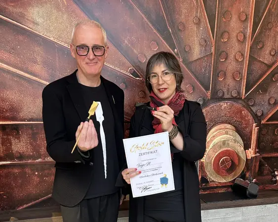 Zwei Personen halten eine Auszeichnung und ein Zertifikat vor industrieller Kulisse.