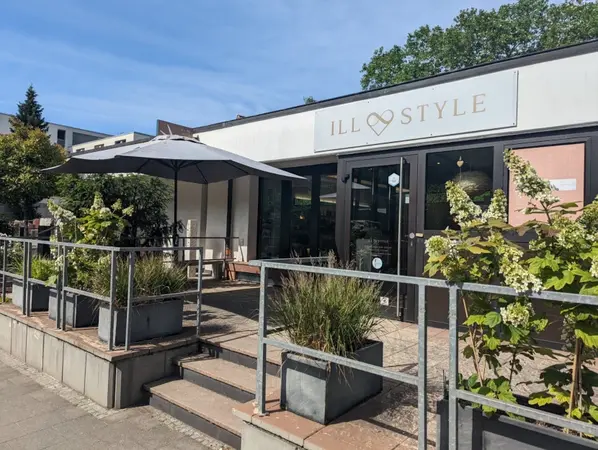 Modernes Café mit Terrasse, Sonnenschirm und Pflanzen vor dem Eingang von ILLSTYLE.