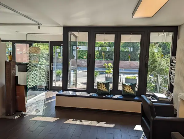 Heller Wartebereich mit großen Fenstern, Pflanzen, Sitzbank und moderner Einrichtung.